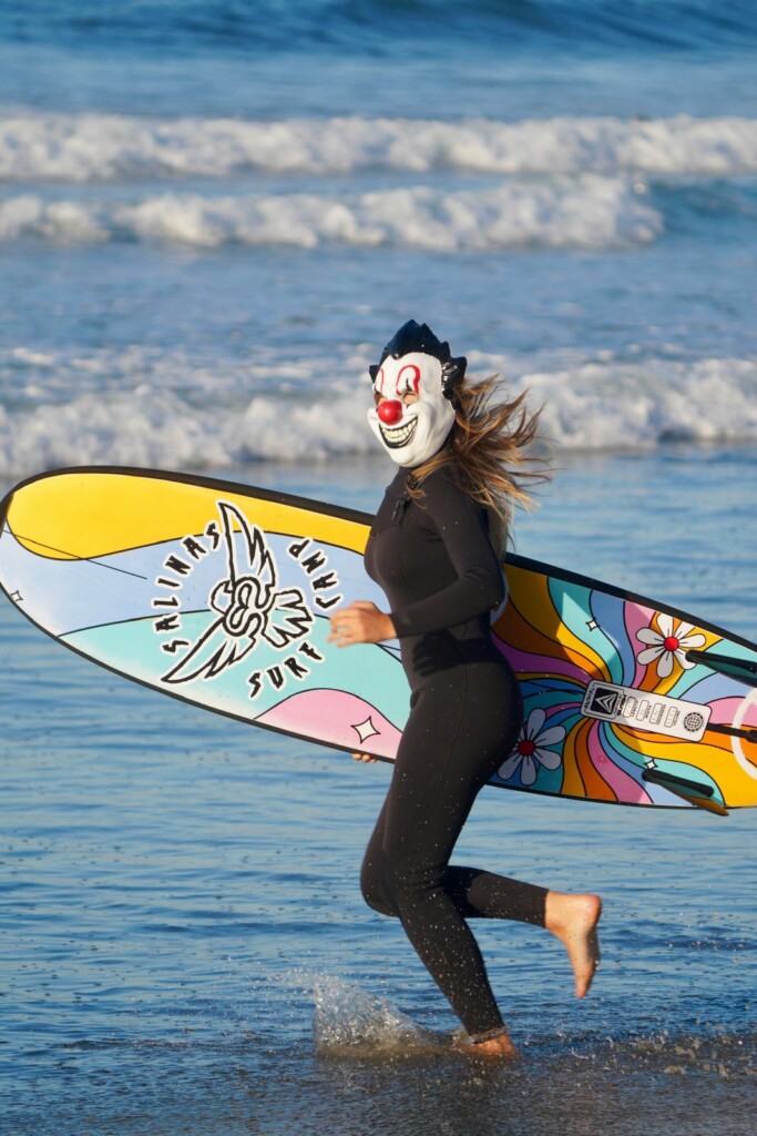 3 Surfista disfrazada de payaso corriendo hacia el agua con su tabla
